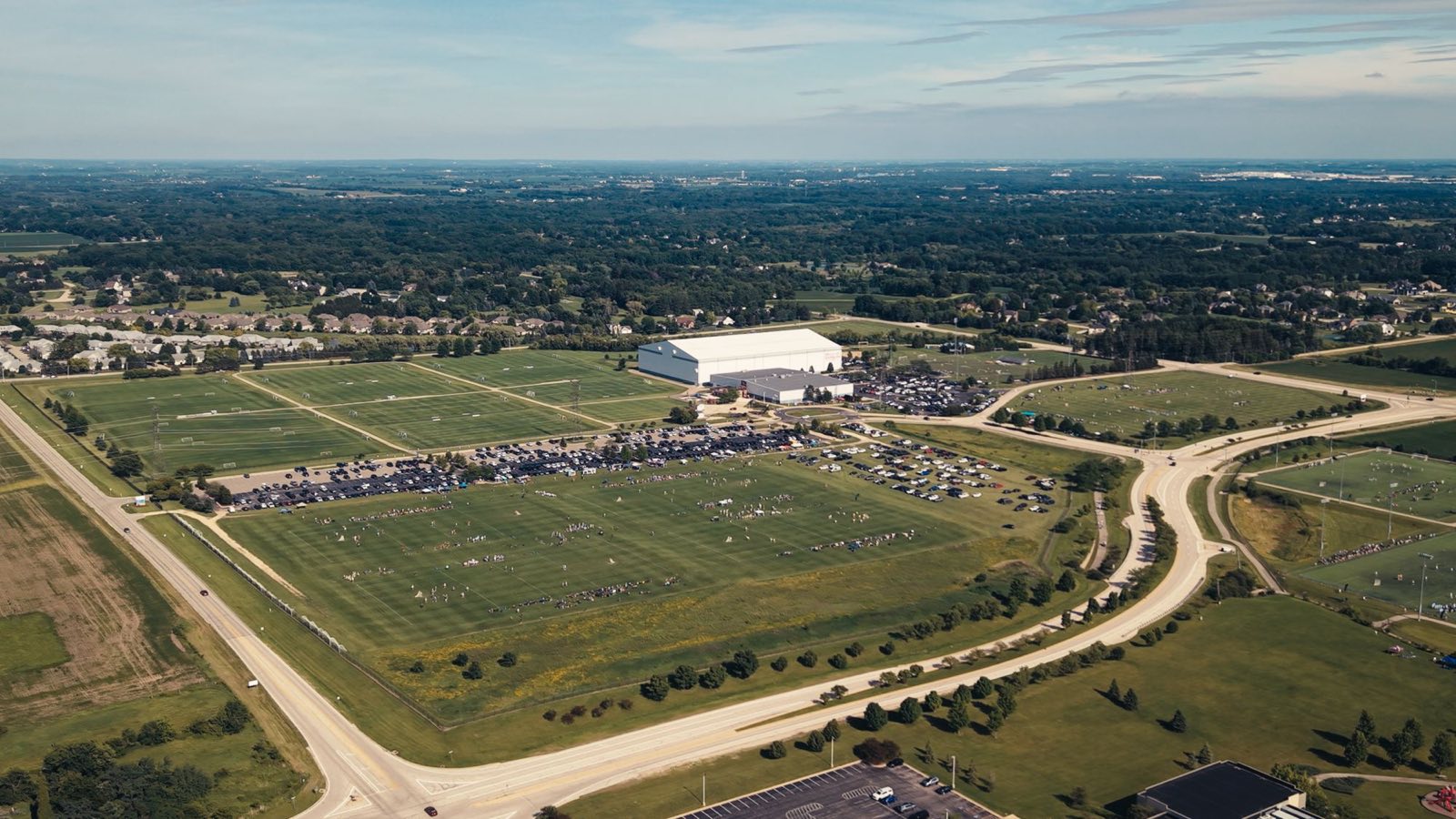 Aerial view of a sports complex on tournament day, with games on every field